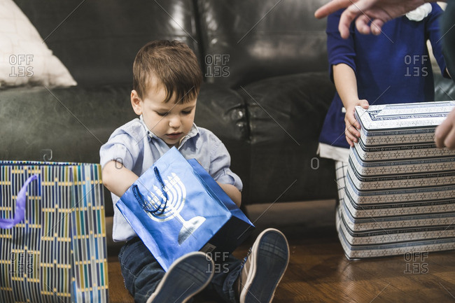 Little boy sitting on a floor opening a gift for Hanukkah