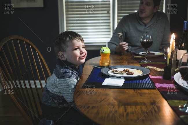 Boy and his father at a dining table with a lighted menorah