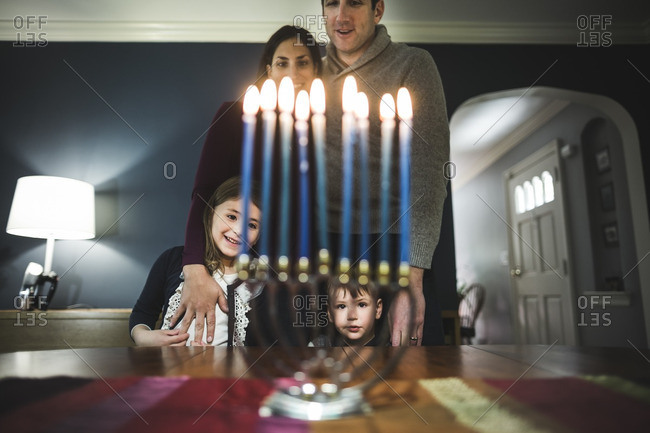 Family of four standing together looking at a lighted menorah