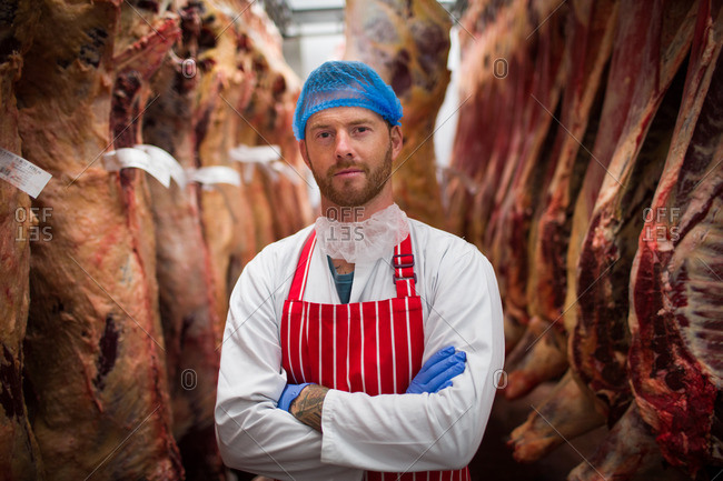 Portrait of butcher standing with arms crossed in meat storage room at butchers shop