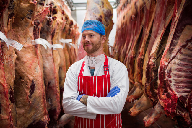 Smiling butcher standing with arms crossed in meat storage room at butchers shop