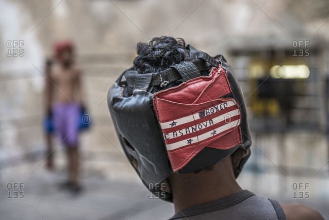 Old Havana, La Habana, Cuba - April 24, 2014: Close-up of a the head and headgear of a young Cuban boy as he prepares to spar with his opponent seen in the background at Project Cuba Boxeo, an aid project from Malaika Aid for Children, the creation of Samuel 'Sammy' Fabbri. The organization brings boxing to Cuban children from 8-21 years of age. His headgear reads "BOXEO CASANOVA", hand written in pen. The boxing ring sits between a group of crumbling buildings between Calle San Jose and Calle Aguila, in Old Havana or Habana Vieja, La Havana, Cuba
