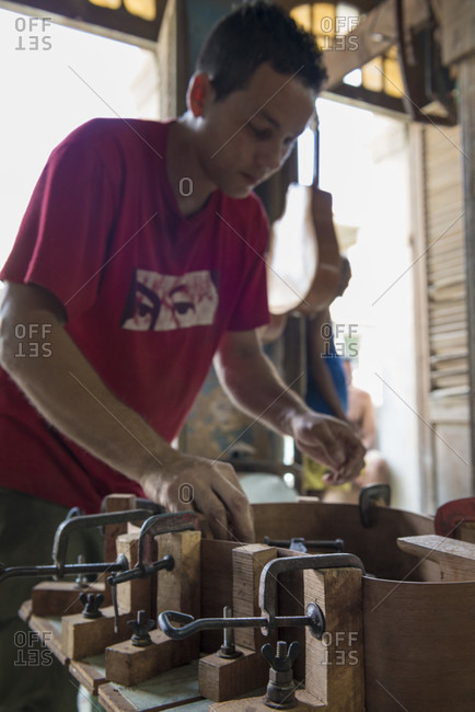 Havana, La Habana, Cuba - April 29, 2014: A young Cuban guitar maker clamping and gluing a guitar together in a hand-made guitar workshop in Havana, La Habana, Cuba