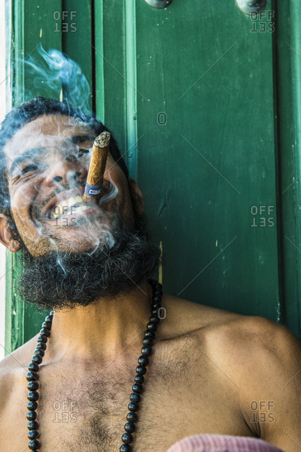 Sancti Spiritus, Cuba - May 1, 2014: A bearded young Cuban artist happily smokes a Montecristo cigar while a puff of smoke surrounds his face. His pose reminds one of Fidel Castro.  Trinidad, Sancti Spiritus, Cuba