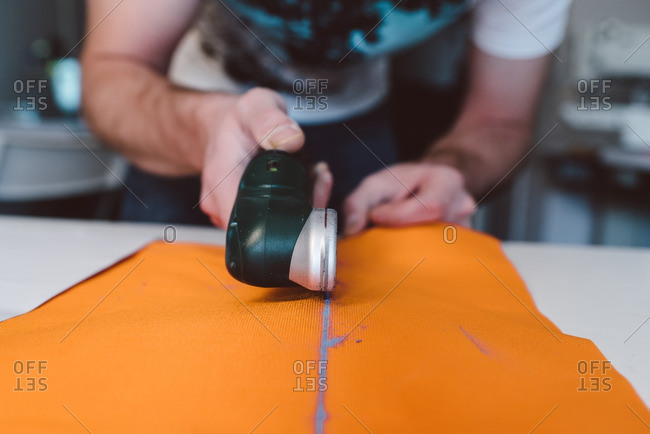 Craftsman using rotary cutting tool on orange fabric