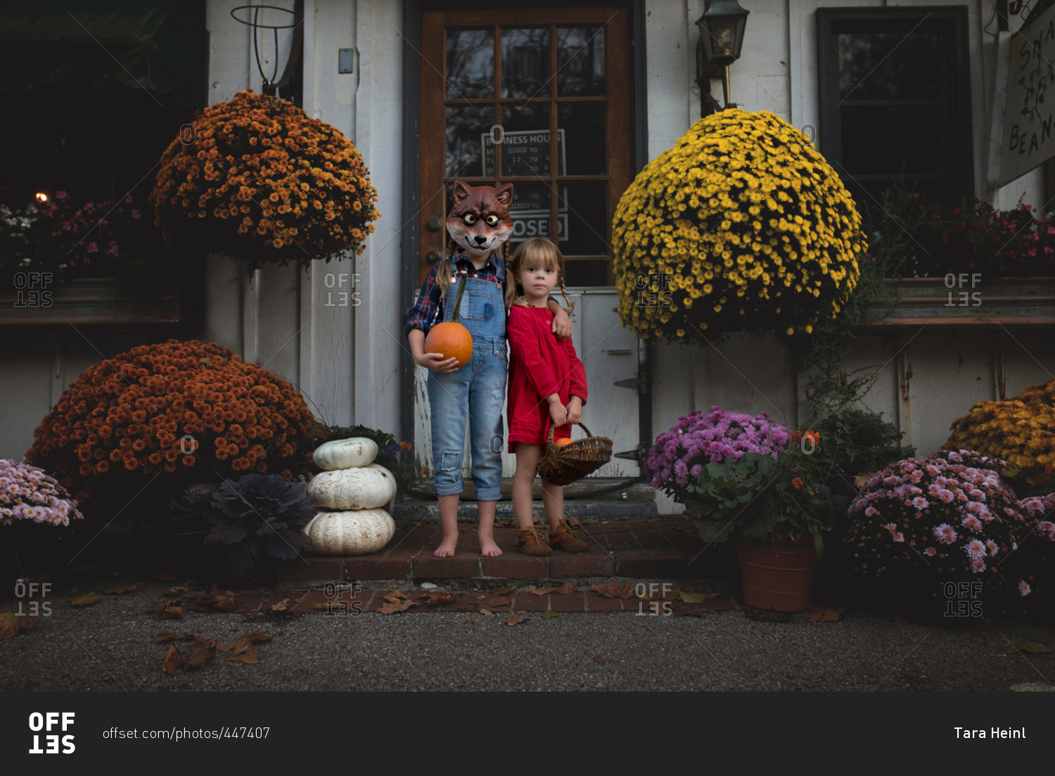 Two young girls holding pumpkins with one wearing a fox mask
