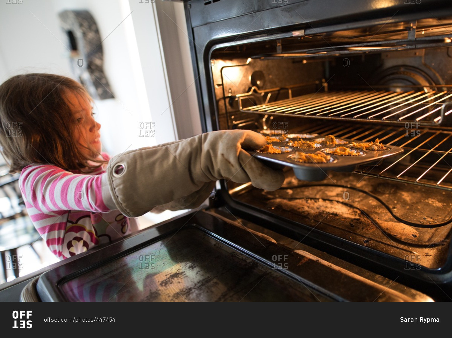 girl-putting-a-muffin-pan-into-an-oven-stock-photo-offset