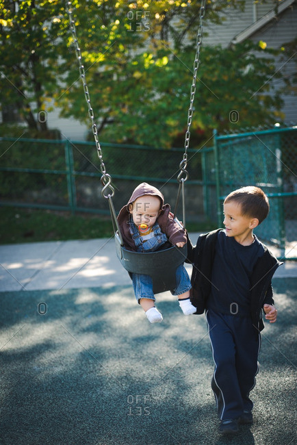 Boy Pushing Baby In Swing Stock Photo Offset