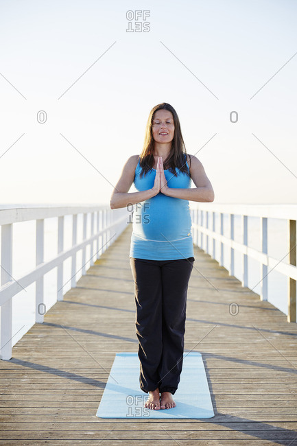 Pregnant woman standing in prayer position on pier against clear sky