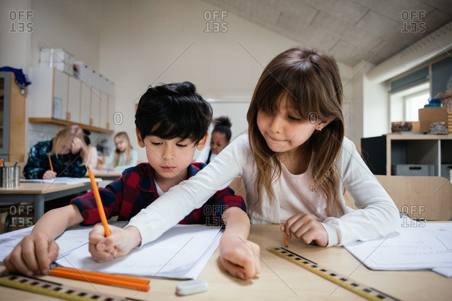 Female friend helping student while studying at desk in classroom