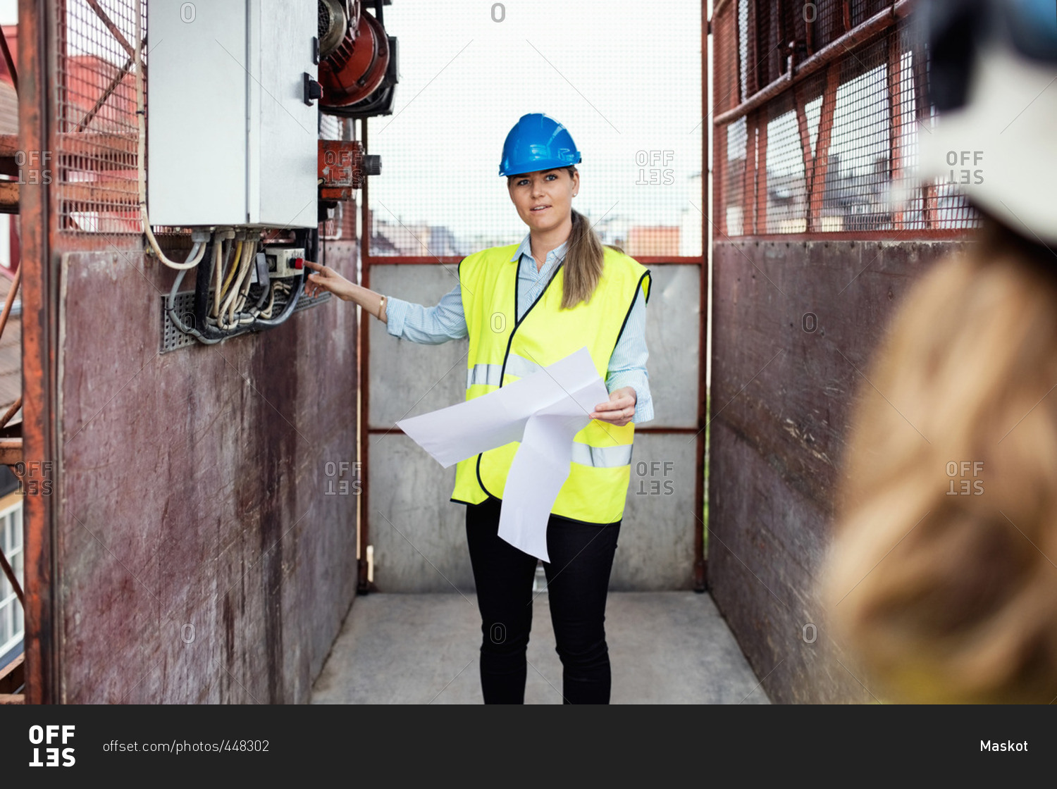 Construction manager holding documents while showing machinery in construction elevator
