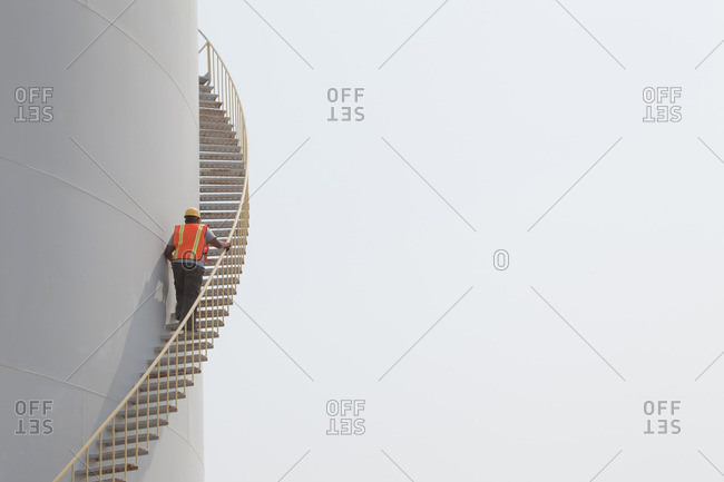 Mixed race worker climbing staircase on storage tank