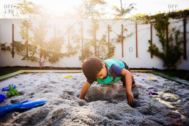 Boy digging in backyard sandbox