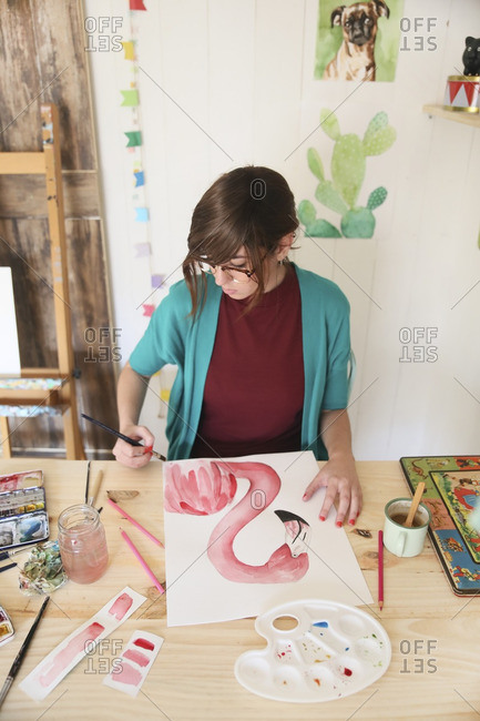Woman painting aquarelle of a flamingo on desk in her studio