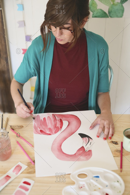 Woman painting aquarelle of a flamingo on desk in her studio
