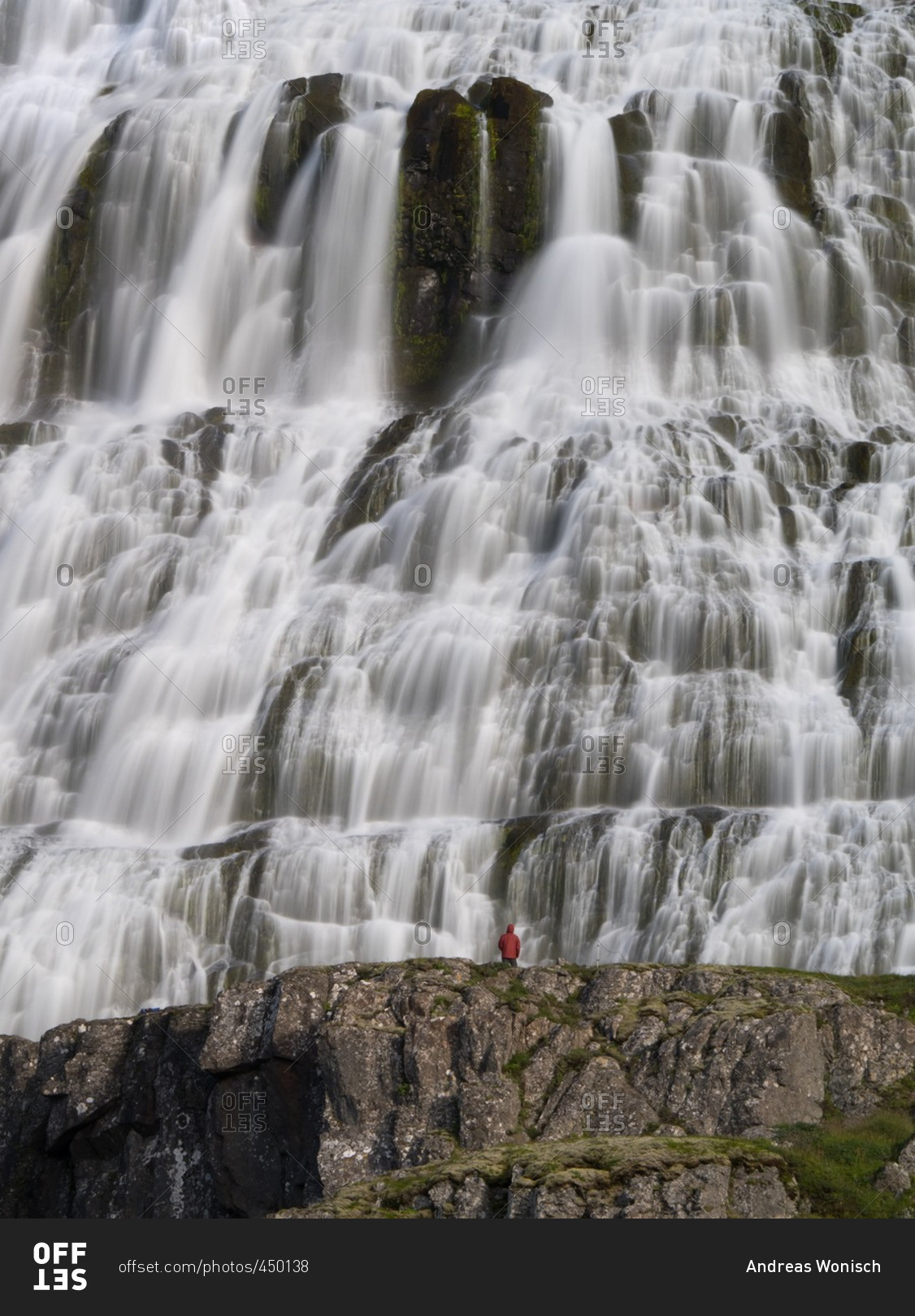Tourist in red raincoat gazing at waterfall in Iceland