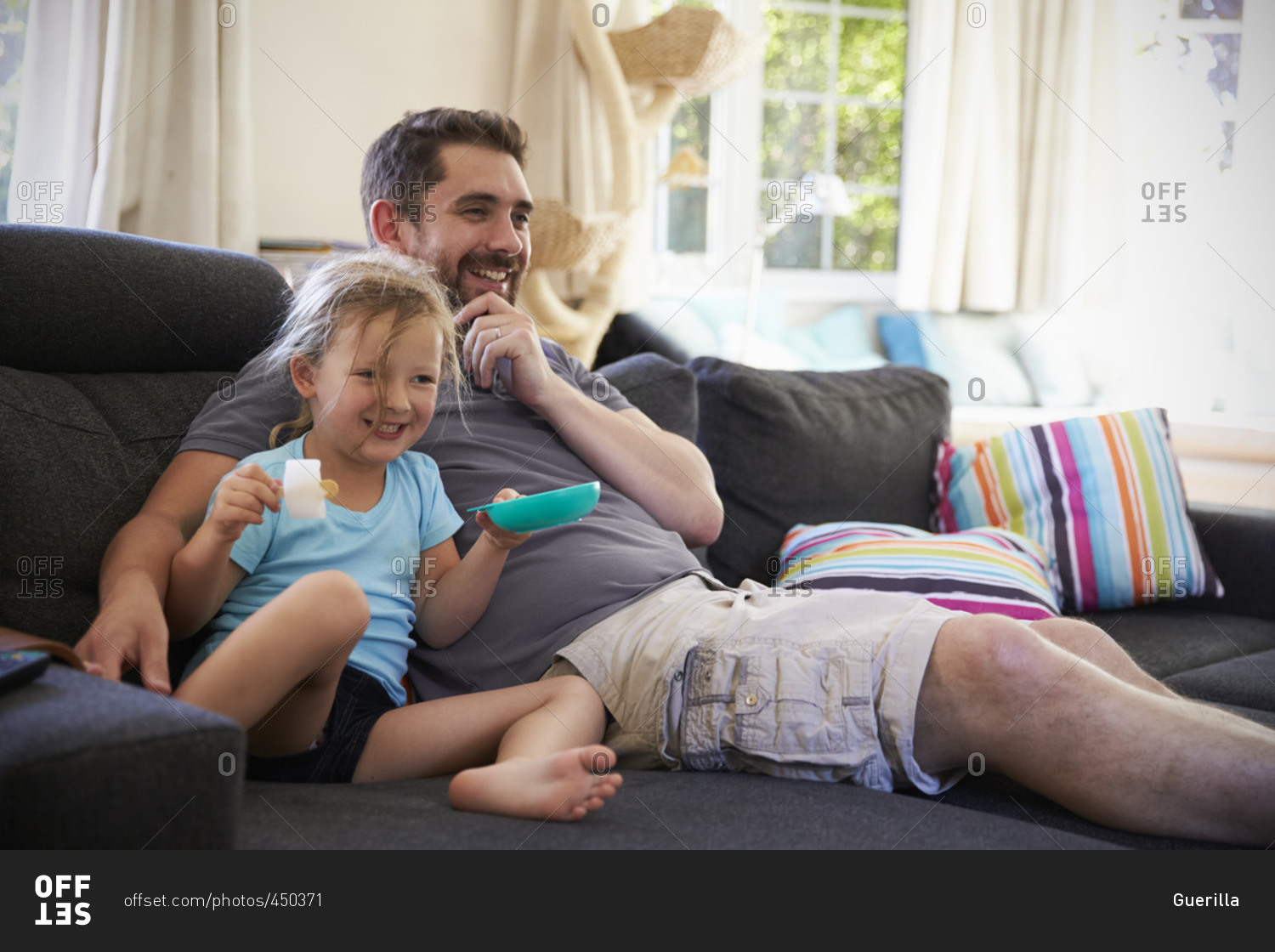 Father and daughter sitting on sofa watching tv together stock photo ...