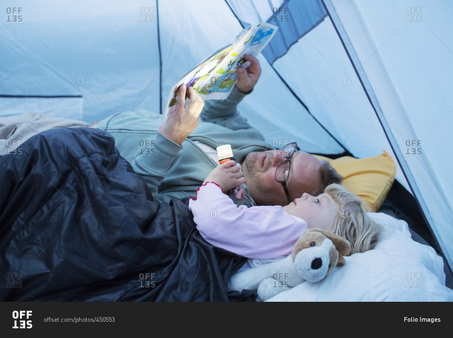 Sweden, Father and daughter reading comic book in tent