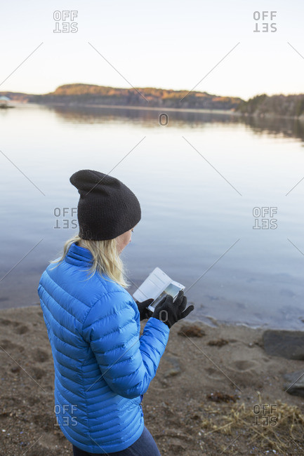 Sweden, Bohuslan, Woman standing with smart phone at Gullmarn fjord