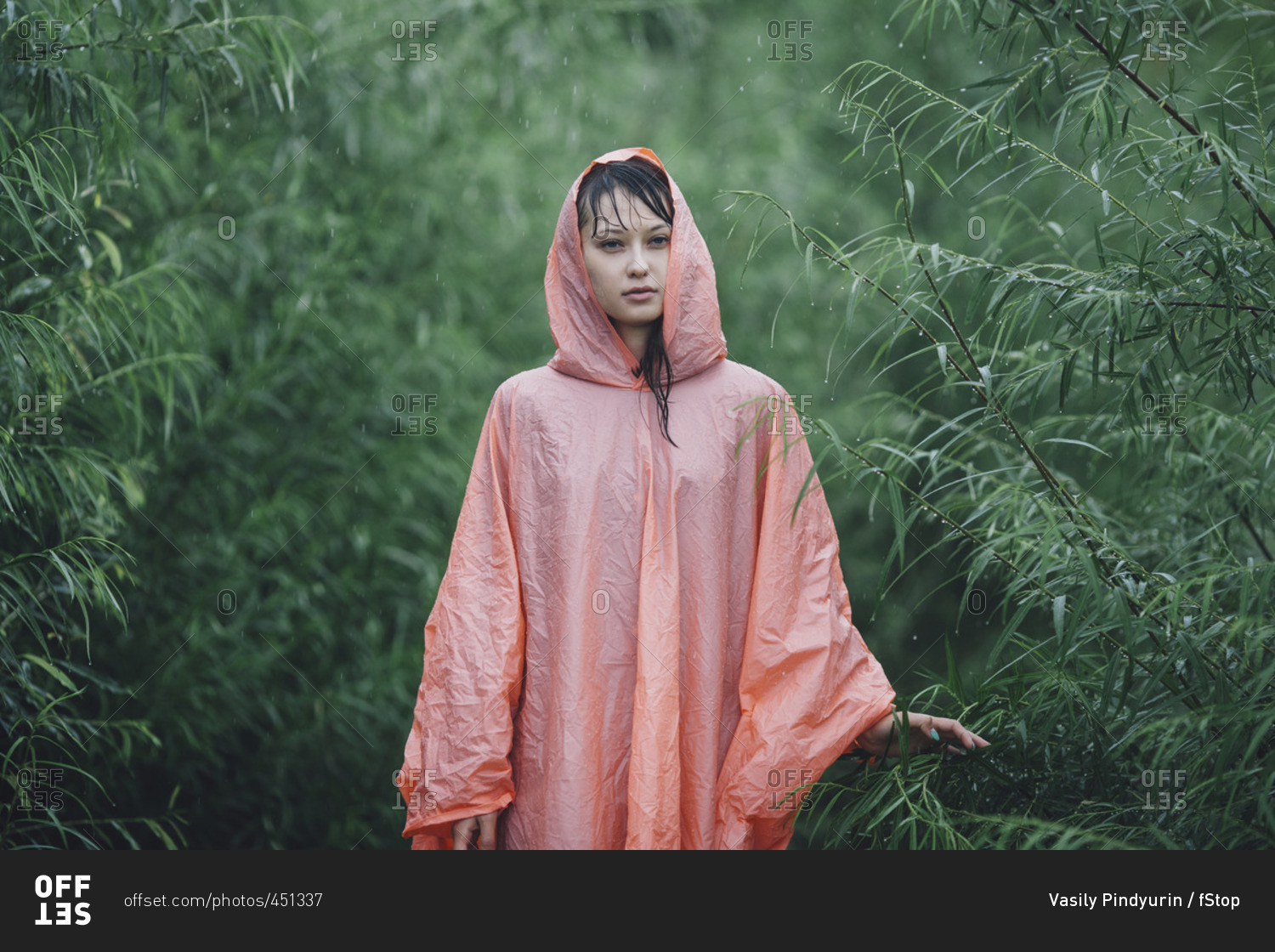 Young woman wearing raincoat standing amidst plants during rainy season