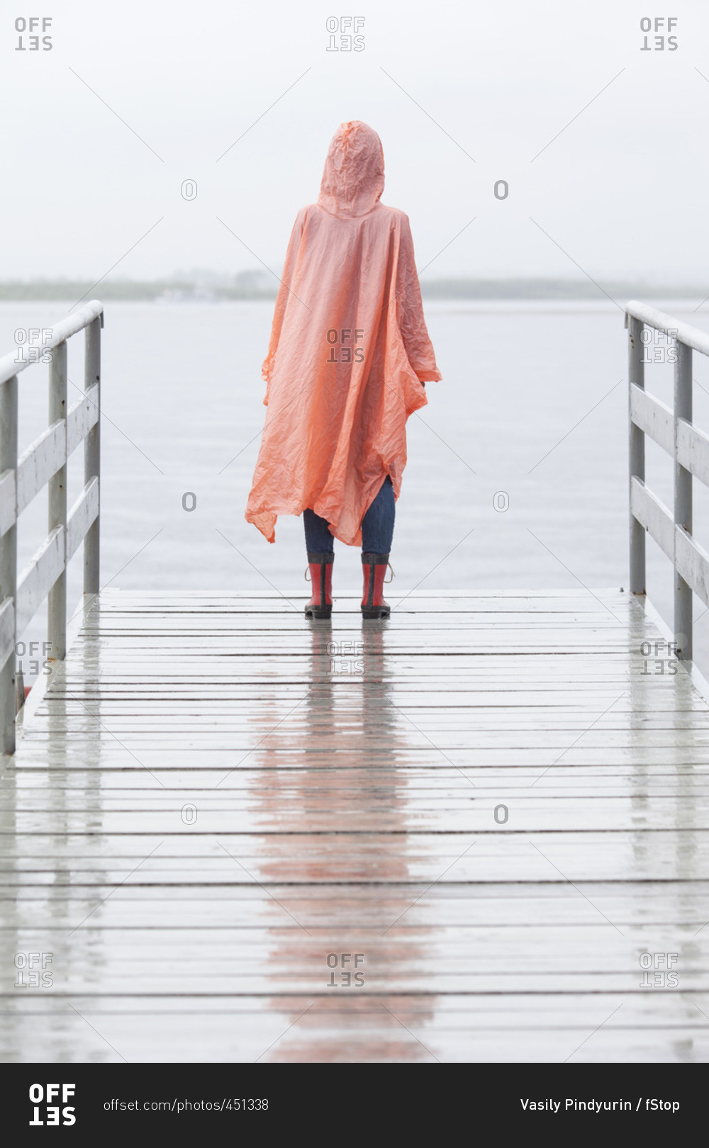 Rear view of woman wearing raincoat standing on jetty during rainy season