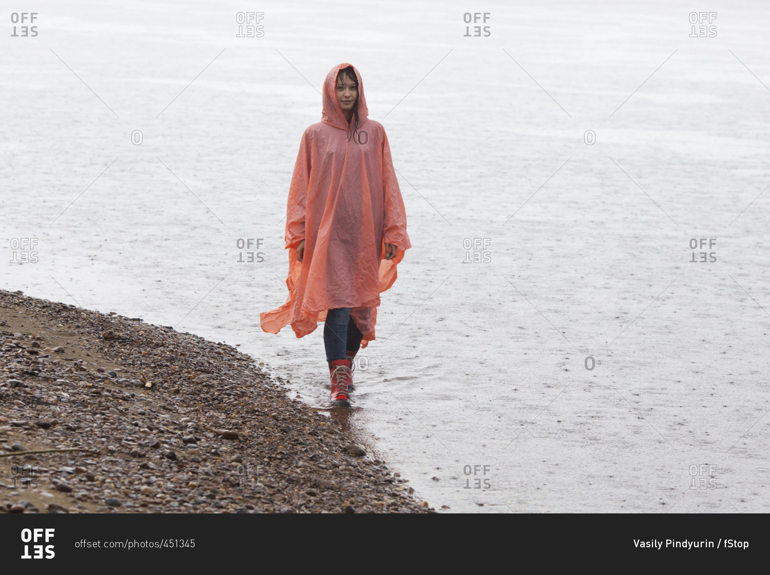 Woman wearing raincoat walking at lakeshore during rainy season