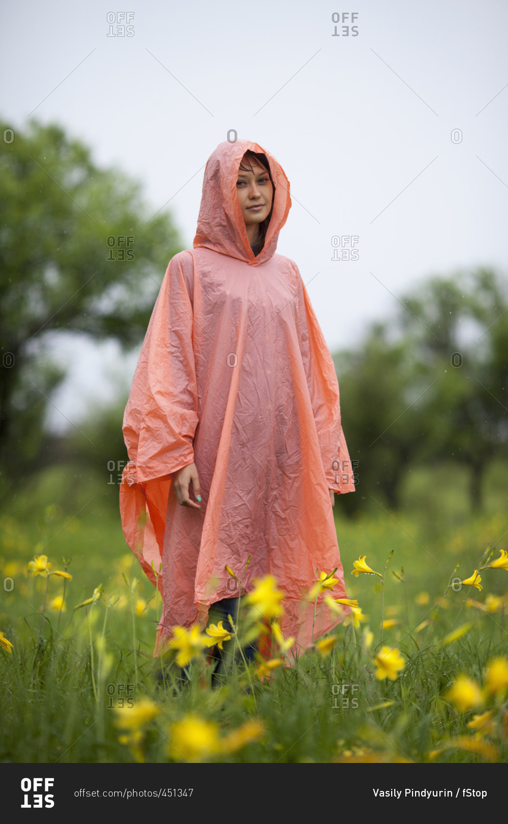 Woman wearing raincoat standing amidst yellow flowering plants in rainy season