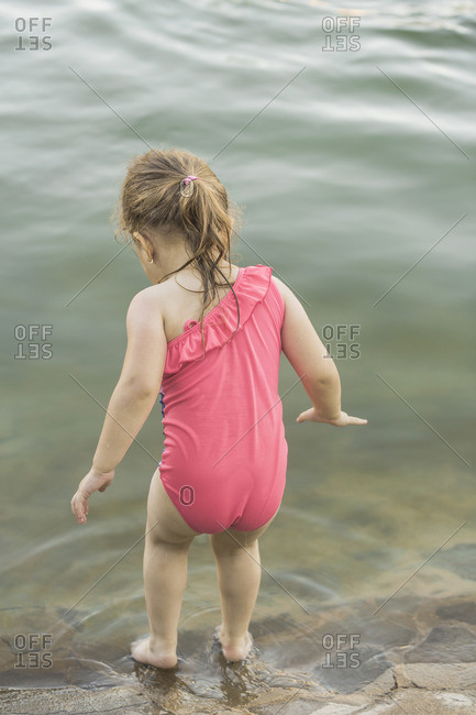 Rear view of girl standing at lakeshore stock photo - OFFSET