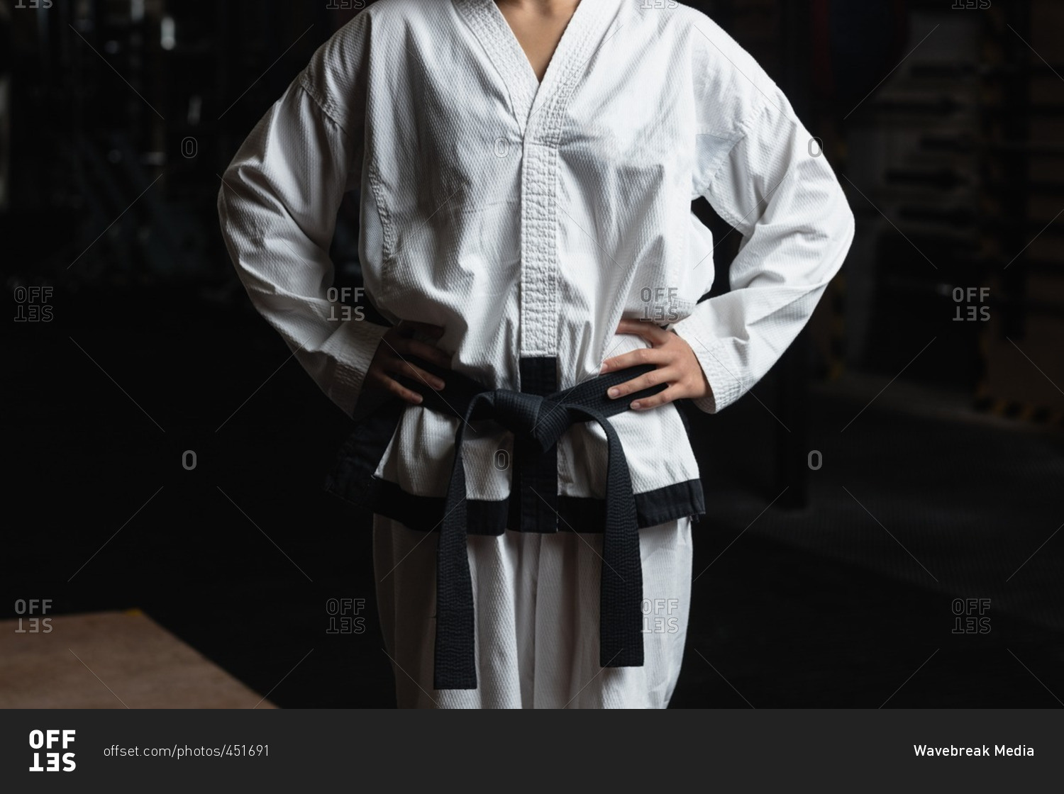 Mid-section of karate woman standing with hand on hip in fitness studio