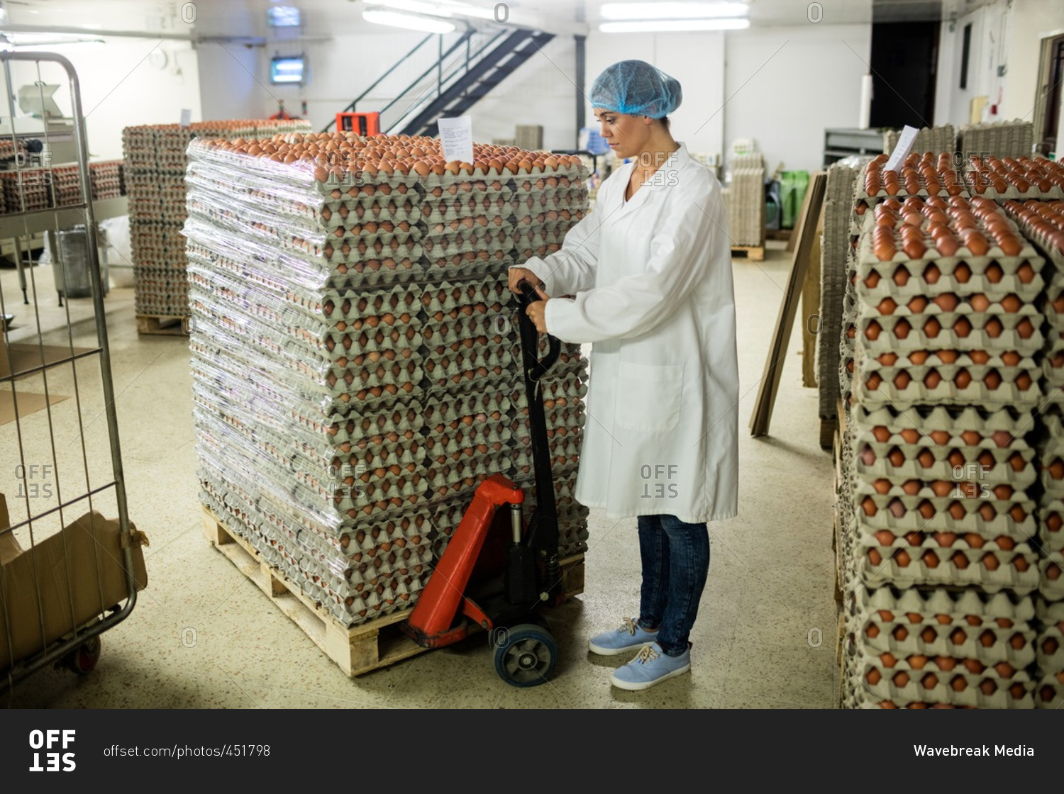 Female staff loading carton of eggs on pallet jack in egg factory