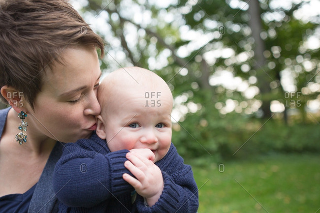 Woman kissing her baby\'s ear outdoors