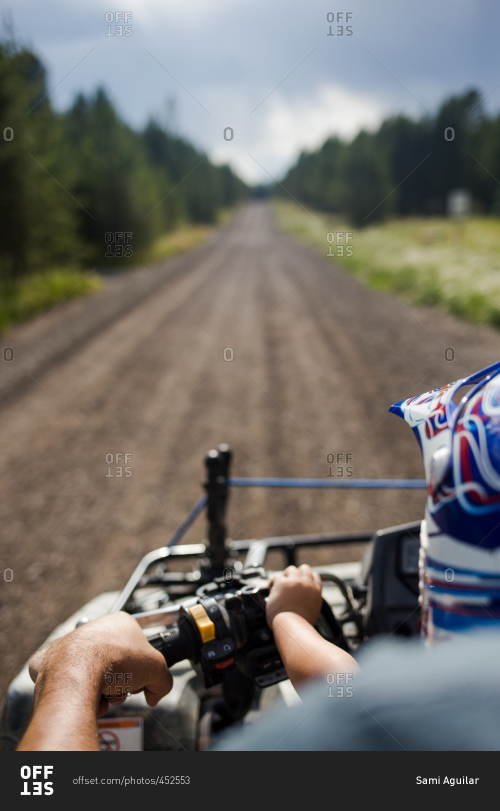 Boy riding four-wheeler with his dad on a long dirt road