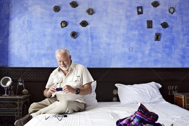 Senior man using smartphone on hotel room bed