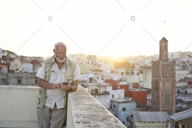 Man using smartphone on terrace at sunset