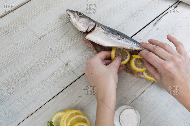 Person stuffing a fish with lemon slices on a wooden table