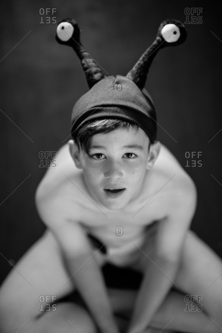Portrait of a young boy sitting cross-legged in an alien hat