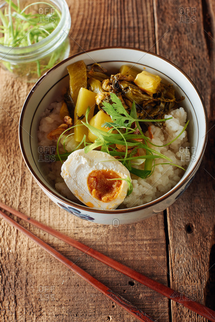 Congee, traditional rice porridge served with 1000 year old duck egg, pickled mustard greens, garlic chips, and cut green onions on a rustic wood table.