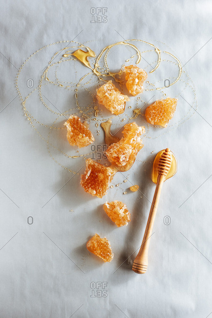Honeycomb and honey spoon with honey drizzled on parchment.