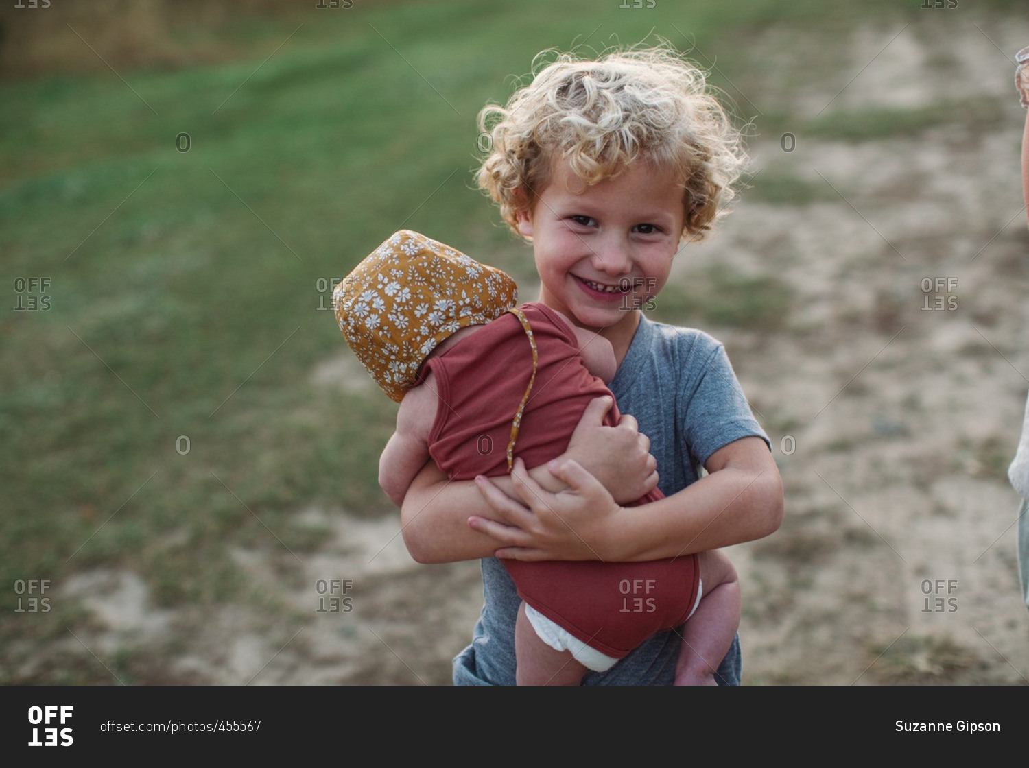 Little boy carrying his baby sister in a field at sunset