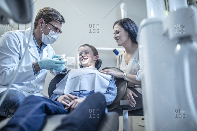 Orthodontist explaining dental mold to boy with mother in dental surgery