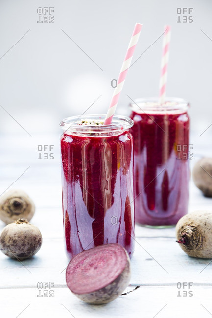 Two glasses of beetroot smoothies with hemp seed and whole and sliced beetroots