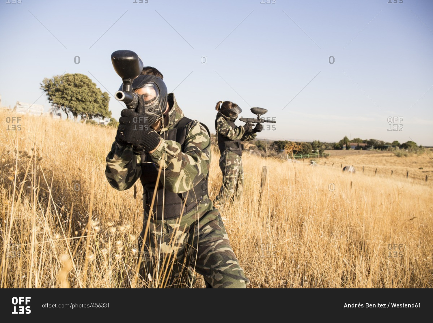 Paintball players in grass aiming with paintball gun during a paintball game
