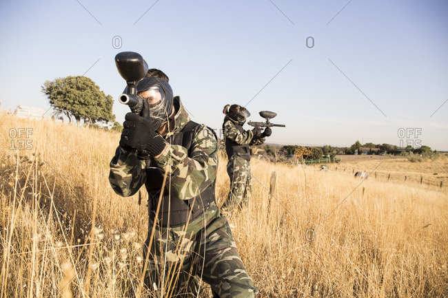 Paintball players in grass aiming with paintball gun during a paintball game