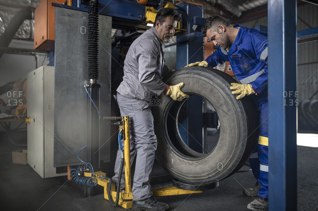 Two tire repairmen lifting tire in factory
