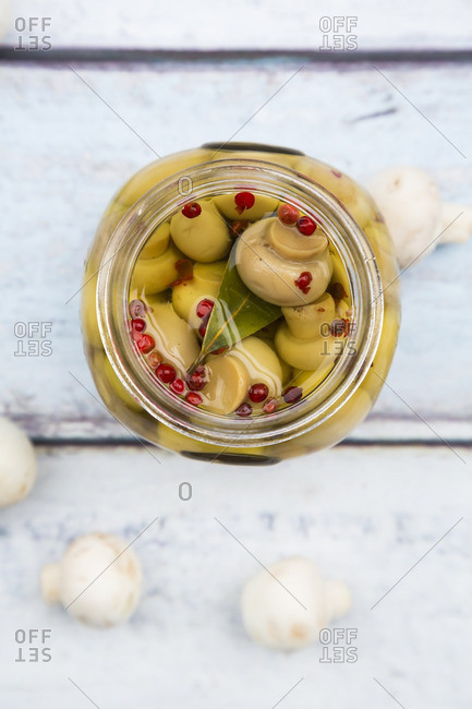 Glass of pickled champignons with red peppercorns and bay leaf- close-up