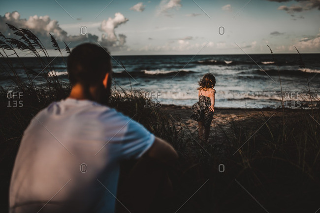 Father watching daughter run on the beach