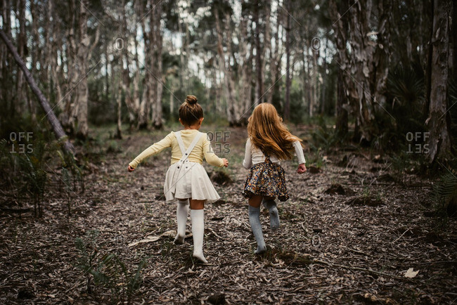 Two little girls running in the woods from behind
