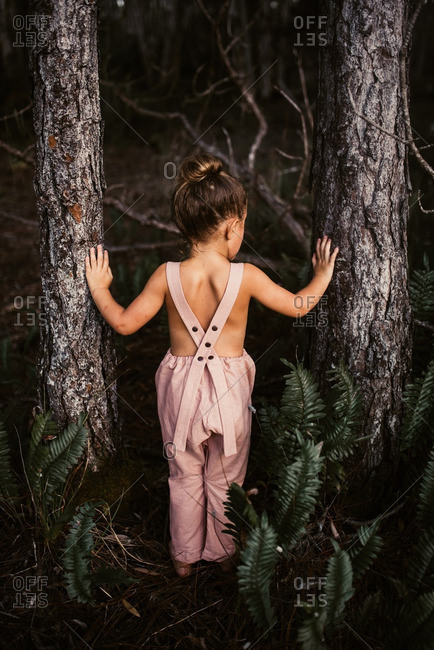 Little girl standing between two trees in the woods