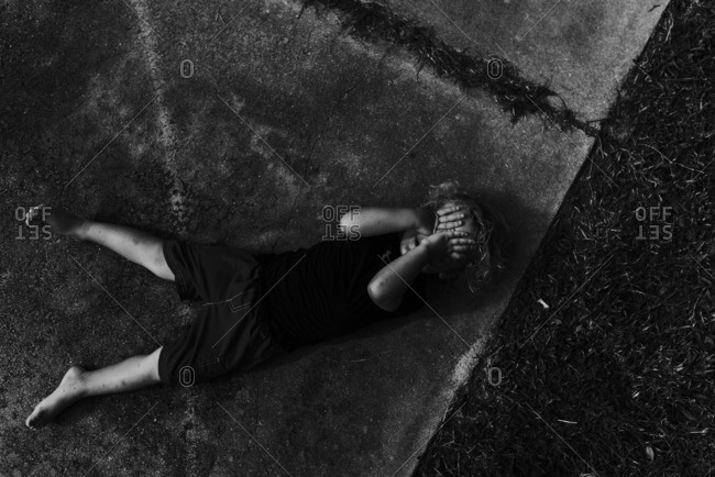 Child lying on the sidewalk covering his face
