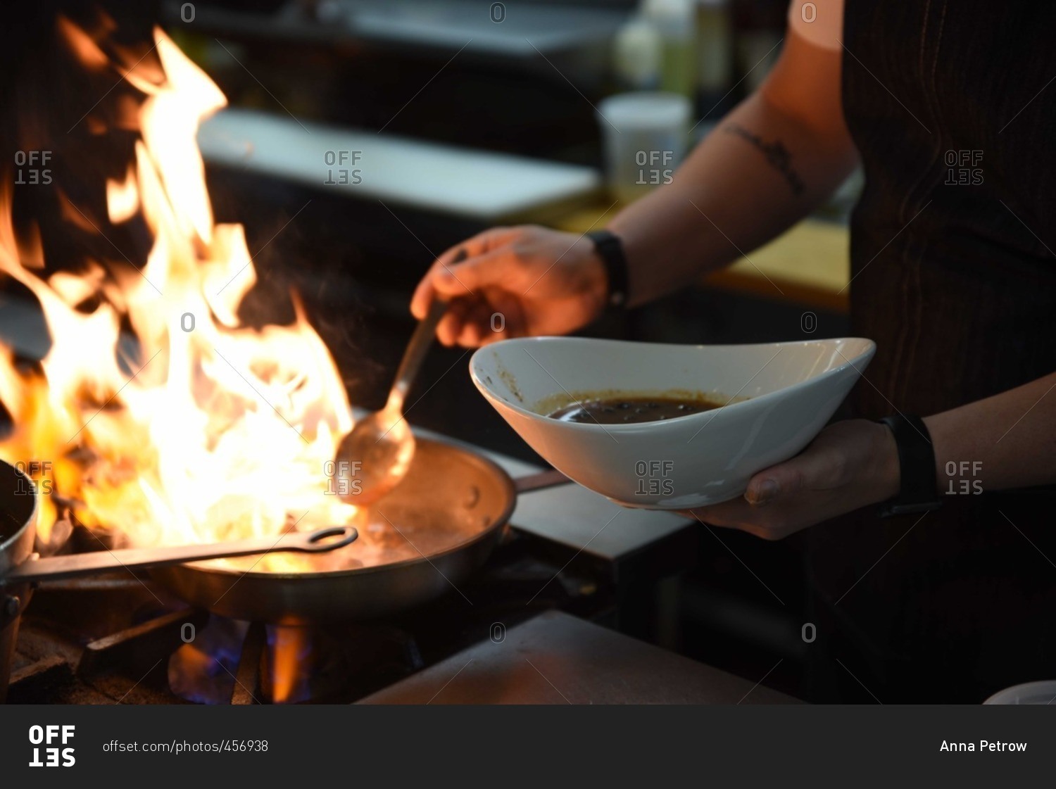 Person adding a spoonful of liquid to a flaming pan on a stove